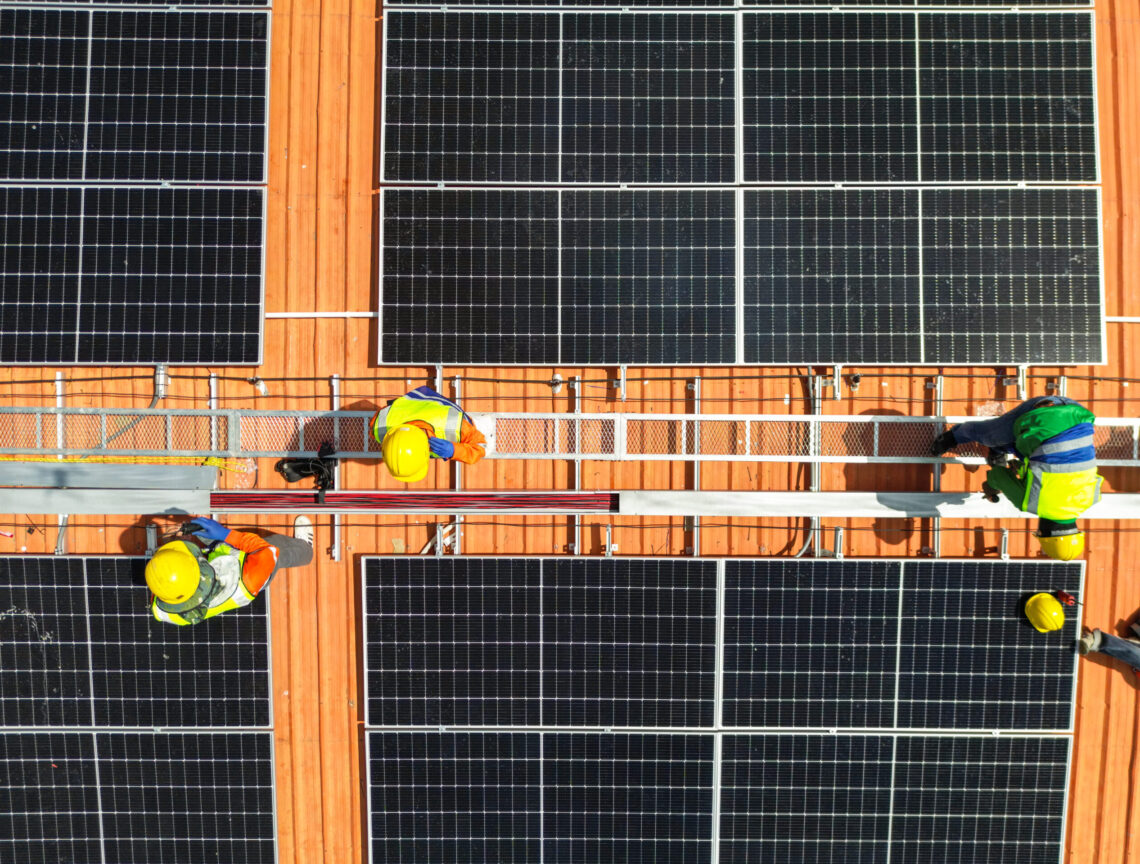 top aerial of engineer men inspects construction of solar cell panel or photovoltaic cell at roof top. Industrial Renewable energy of green power. factory at urban area. worker working on tower roof.
