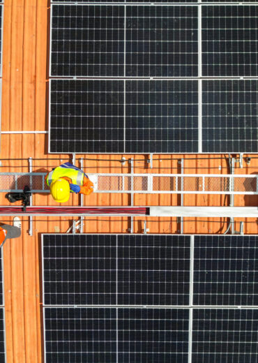 top aerial of engineer men inspects construction of solar cell panel or photovoltaic cell at roof top. Industrial Renewable energy of green power. factory at urban area. worker working on tower roof.